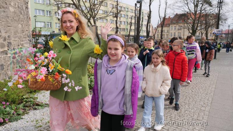 grupa dzieci z panią niosącą kosz kolorowych kwiatów